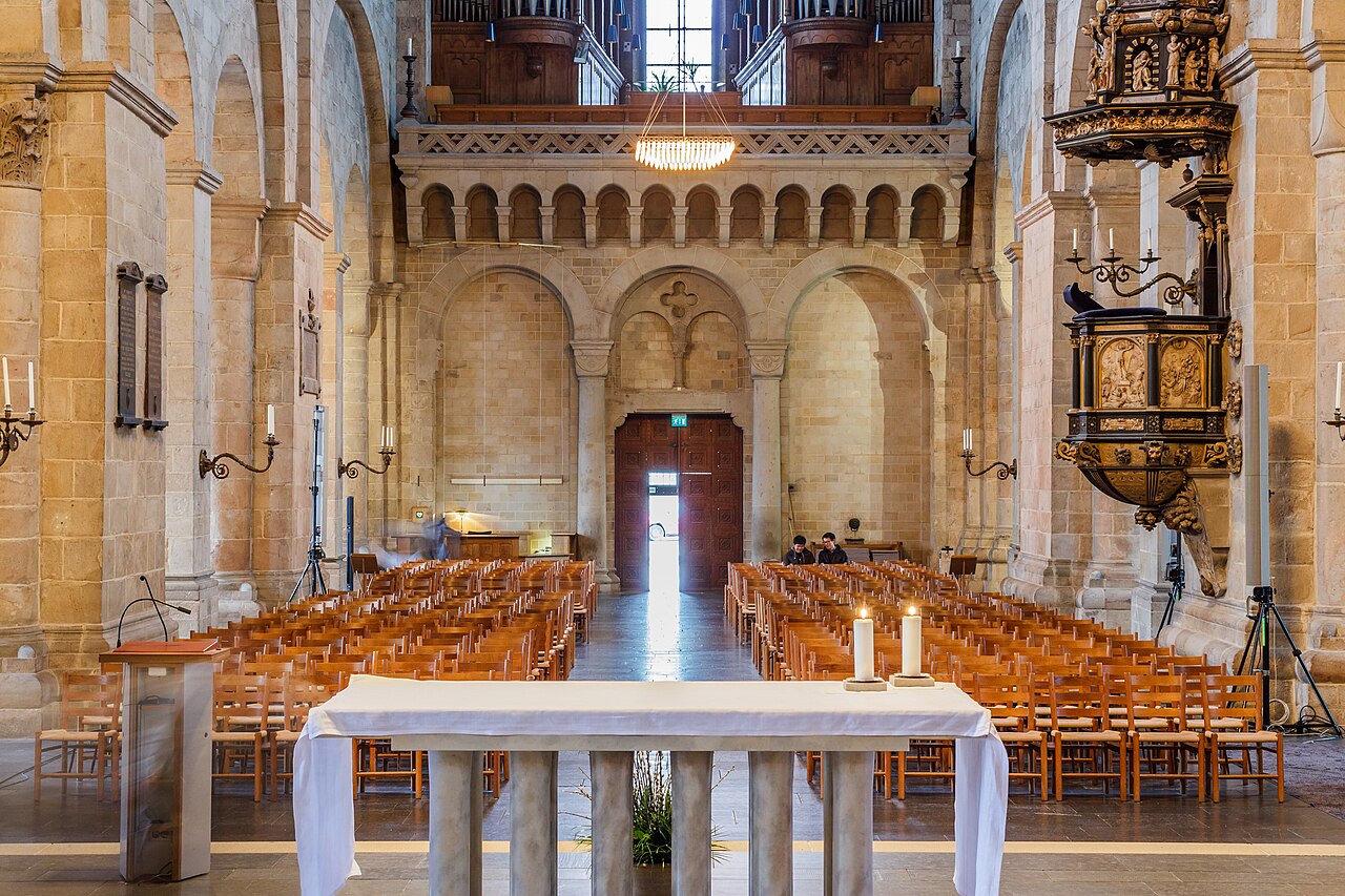 Ljus faller in genom valven i Lunds domkyrka. Kyrkbänkar och altare fyller det stora kyrkorummet.